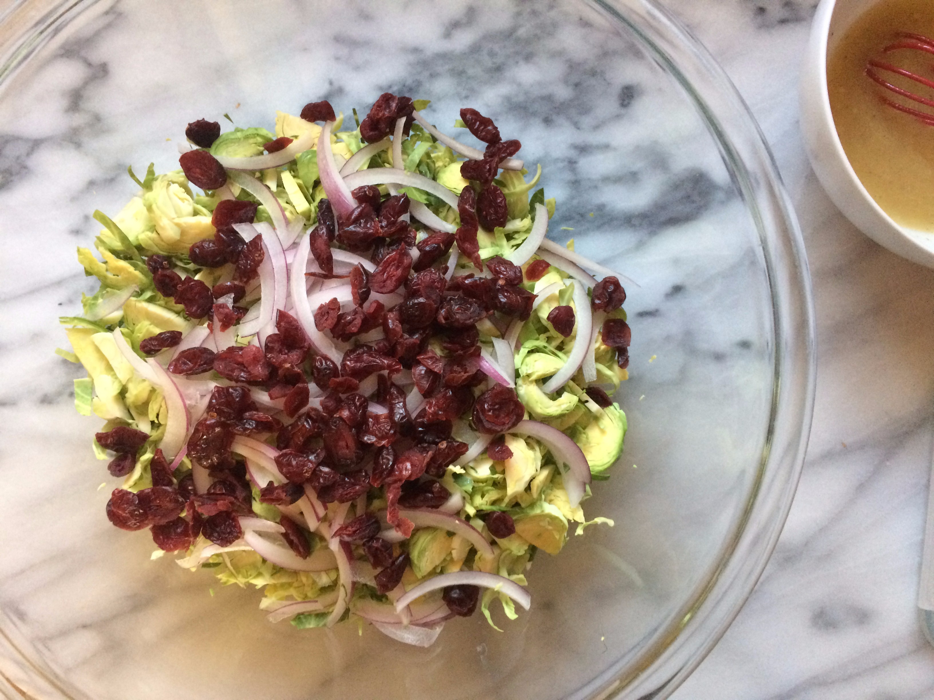Shredded Brussels sprouts, dried cranberries, and red onion in a big bowl with bacon vinaigrette