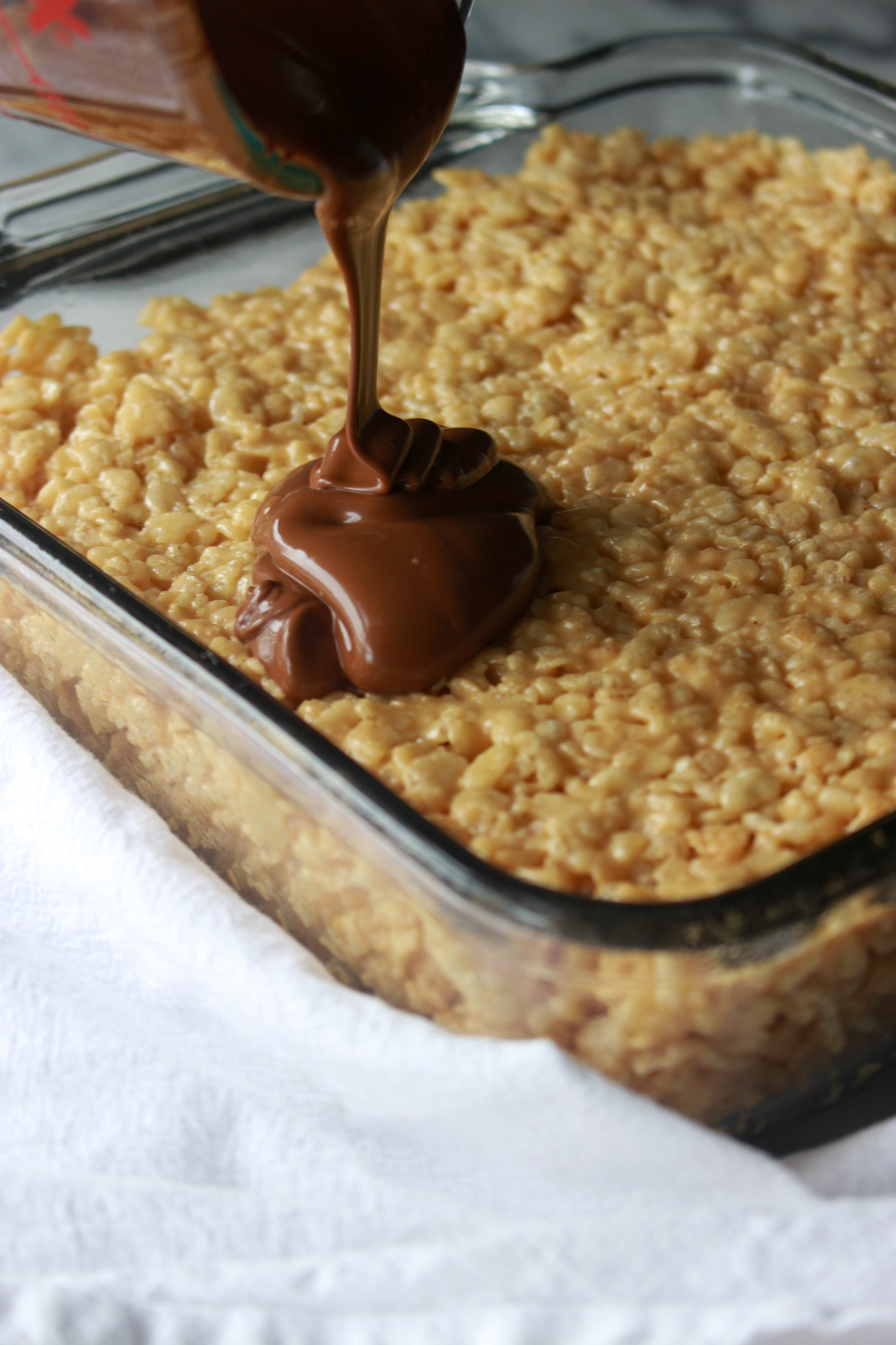 pouring butterscotch+chocolate onto peanut butter rice crispies