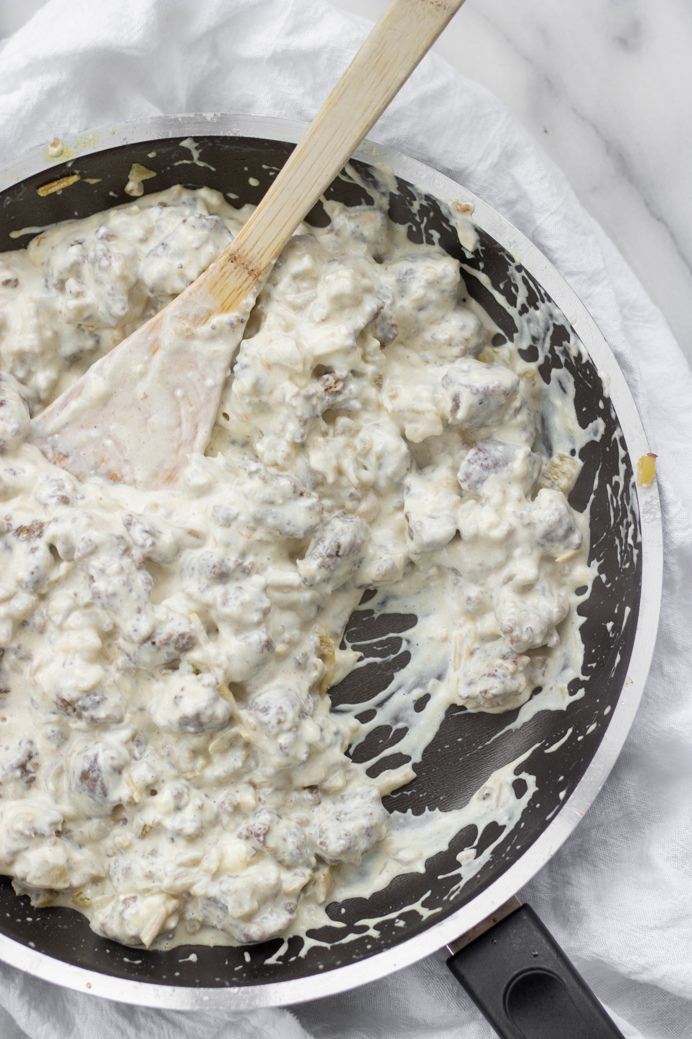 Sausage crumbles and green chiles with melted cream cheese in skillet.