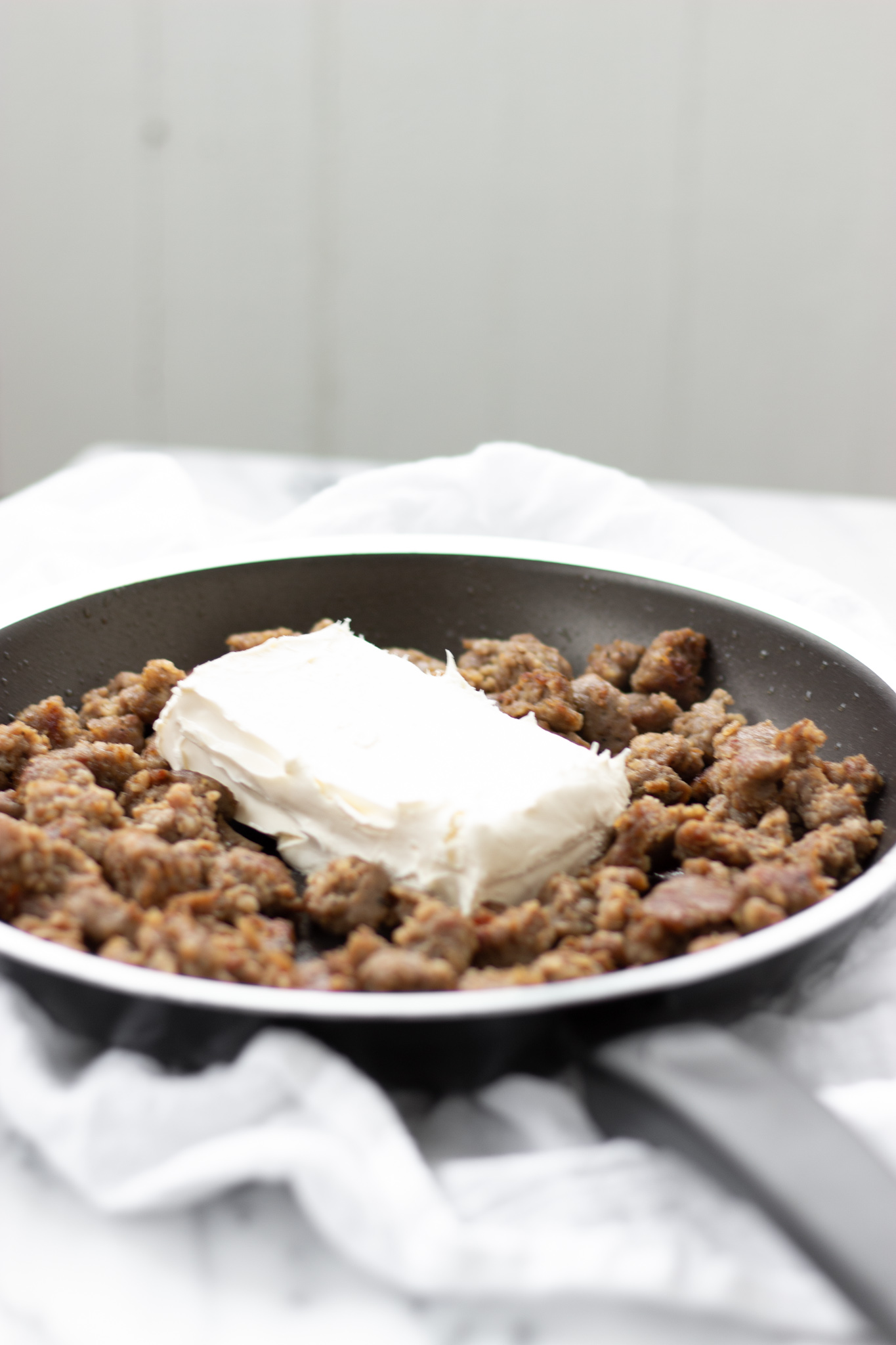 Sausage crumbles in skillet with brick of cream cheese on top.