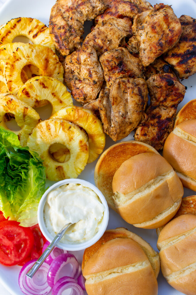 platter of jerk chicken burger toppings, buns, and jerk chicken
